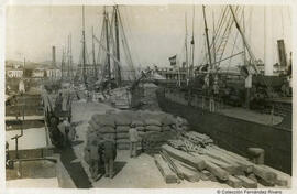 Málaga, barcos amarrados al muelle del puerto y faenas de carga o descarga. Autor desconocido.