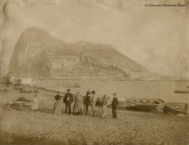 Gibraltar desde La Línea de la Concepción con personajes en la playa, tras los cuales se observa un establecimiento de baños. Fotógrafo desconocido.