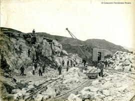 Escena de obras con una grua, raíles y operarios moviendo piedras, posiblemente provincia de Málaga. Fotógrafo desconocido