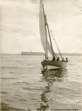 Málaga, barca con una vela latina desplegada junto al morro del puerto. Fotógrafo desconocido.