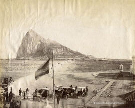 La Línea (Cádiz), plaza de Europa con transeúntes y carruajes en el puesto fronterizo con Gibraltar, campo neutral y Peñón al fondo. Dautez.