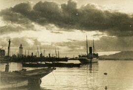 Málaga, barcos de vapor y botes de remo en el interior del puerto en un paisaje nublado. Fotógrafo desconocido.