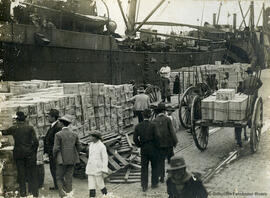 Málaga, muelle de carga en el Puerto con cajas de mercancías junto a los barcos, carros, transeuntes curiosos y operarios. Foto Greco.